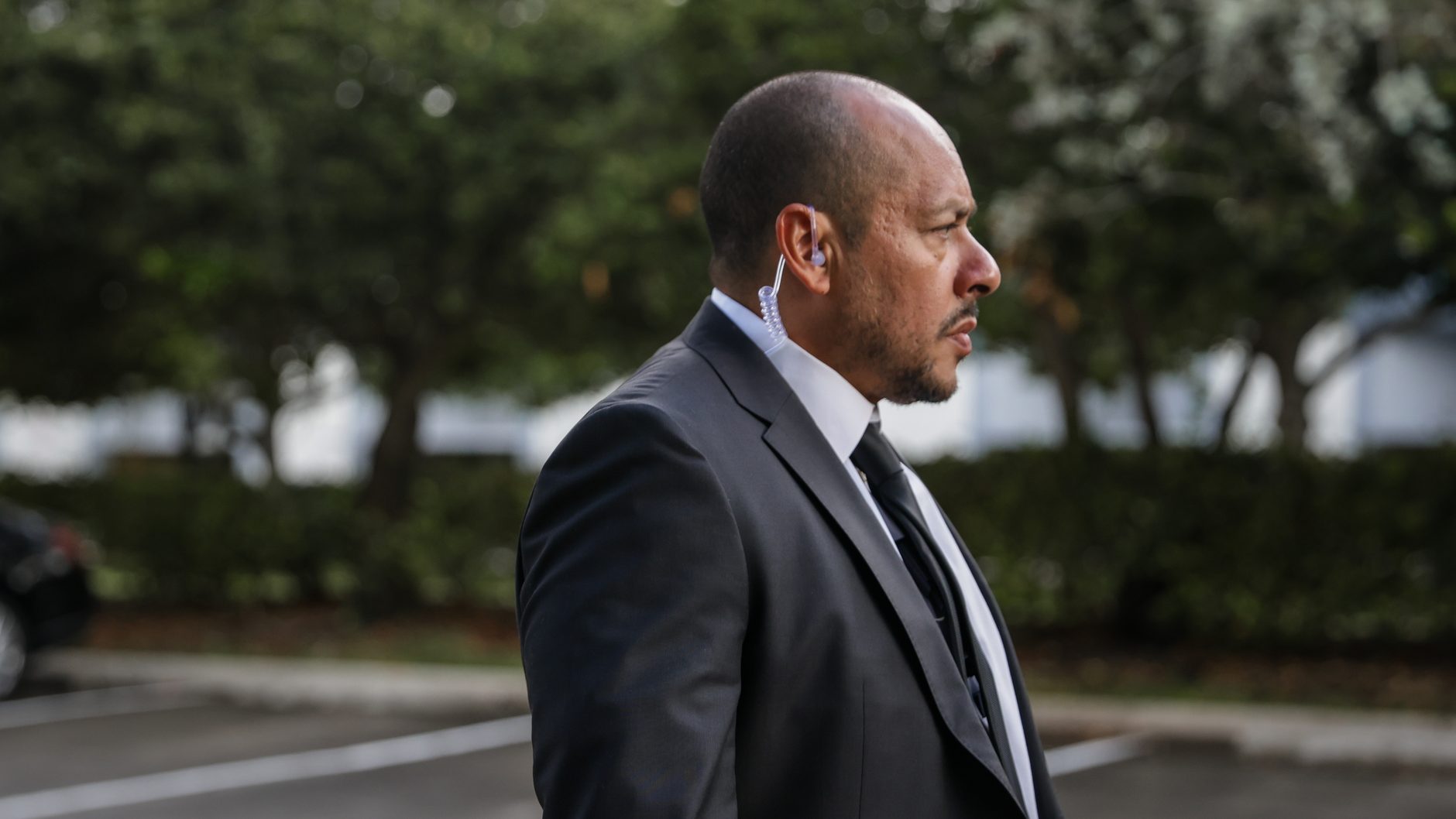 An ARDENT Agent standing quietly outside a meeting room in business dress, at a distance.